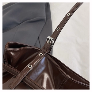 Detail of adjustable silver buckle and metal eyelets on dark brown glossy shoulder bag