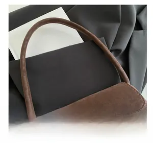 Detail of dark brown suede handbag featuring minimalist gold metal clasp and arc handle