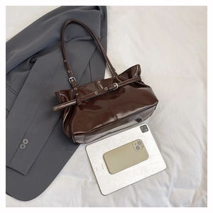 Macro detail of glossy chocolate brown patent leather tote bag with metal buckles