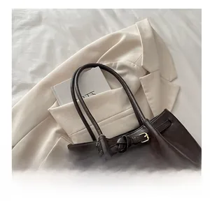 Close-up of a dark brown large tote bag featuring a plush charm and gold buckle detail