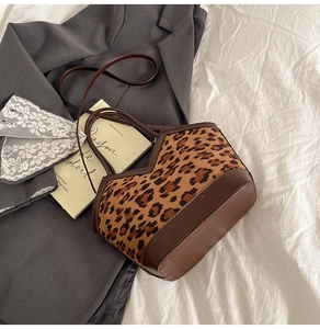 Detail of suede leopard print tote bag with brown leather handles on soft bedding
