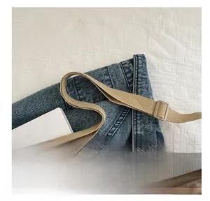 Dettaglio della tracolla regolabile in tela beige su borsa a tracolla in denim blu