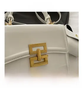 Close-up of white leather handbag featuring a golden geometric lock and refined stitching