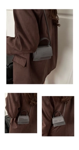 Detail of grey patent leather square crossbody bag worn by a model in brown suit