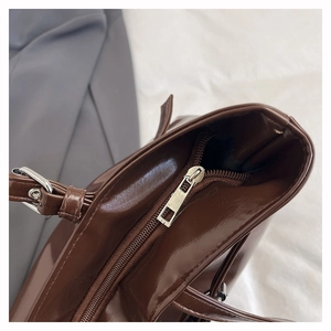 Detail of a dark brown glossy leather shoulder bag with metallic zipper and adjustable strap