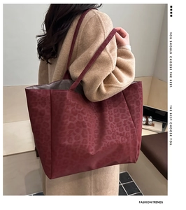 Detail of burgundy leopard embossed tote bag worn over the shoulder showing large capacity