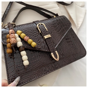 Detail of dark brown crocodile embossed crossbody bag with golden buckle and beaded tassel
