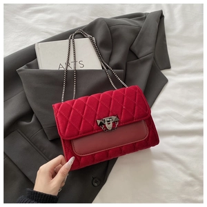 Detail of red quilted velvet bag with chain strap resting on a gray suit jacket