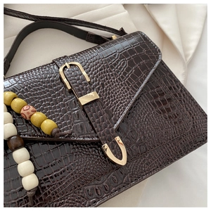Close-up of brown crocodile embossed leather bag with gold buckle and beaded charm