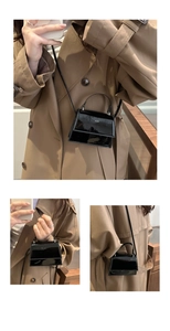 Detail of a mini black patent leather handbag with silver hardware and sleek shoulder strap