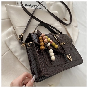 Close-up of brown crocodile pattern handbag with retro beaded tassel and metal buckle