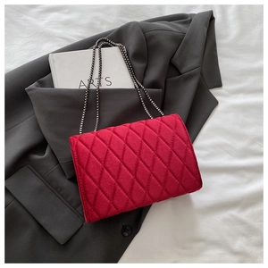 Macro detail of red velvet quilted handbag texture with dark metal chain strap