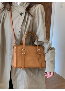 Primo piano di borsa a tracolla opaca marrone con fibbie su un trench coat beige