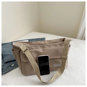 Detail of khaki nylon tote bag showing the fashion label and large capacity next to a phone
