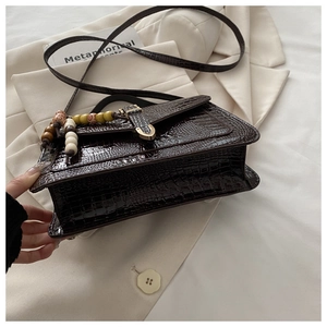 Detail of dark brown crocodile texture bag with metal clasp and colorful beaded charm
