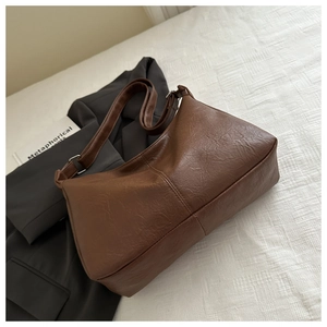 Gros plan d'un cabas vintage marron avec texture cuir et bandoulière réglable sur lit blanc