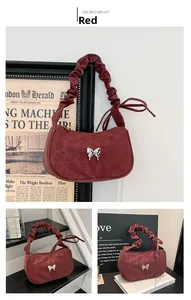 Detail of red suede shoulder bag with pleated handle and silver metal butterfly ornament