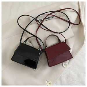 Close-up of minimalist mini flap crossbody bags in glossy black and wine red leather