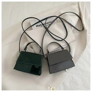 Close-up of mini glossy crossbody bags in dark green and taupe on a white blazer