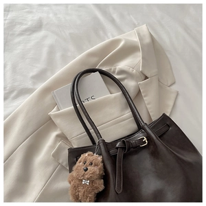 Detail view of coffee brown tote bag with plush bear charm and gold buckle on a blazer