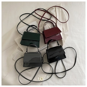 Flat lay of four glossy patent leather mini handbags in dark green, red, grey, and black