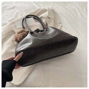 Close-up of a large dark brown tote bag with leather texture and a plush bear pendant