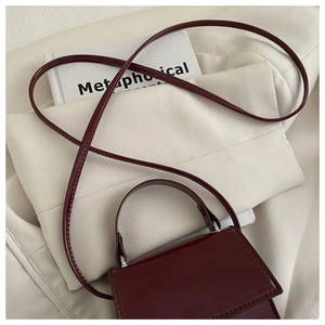 Detail of burgundy rectangular flap bag in glossy leather with silver metal hardware