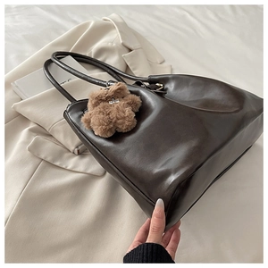 Detail of a dark brown large tote bag with a cute plush bear charm on a white suit
