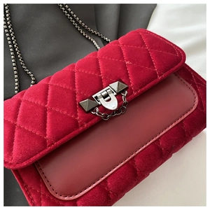 Detail of red velvet crossbody bag with quilted patterns and black metal chain strap