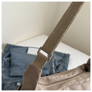 Detail of adjustable woven shoulder strap and plastic buckle on beige nylon crossbody bag