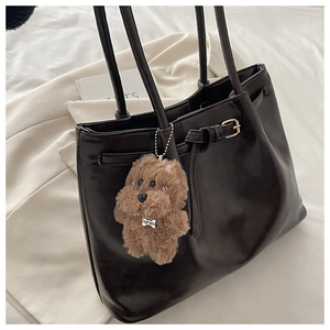 Detail of a black leather tote bag with long straps and a plush brown dog charm