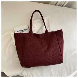 Flat lay of a large burgundy leopard print tote bag with thin straps on a white background