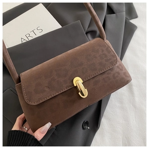 Detail of a brown suede shoulder bag with a vintage gold metal clasp and flap closure