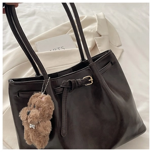Detail of coffee brown tote bag featuring decorative buckle strap and plush dog charm