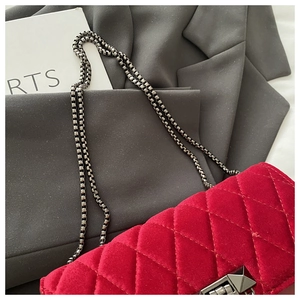 Close-up of red velvet quilted bag with metal chain strap and pyramid stud lock detail