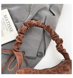 Détail du sac à main en daim marron avec une poignée plissée sur un livre d'art