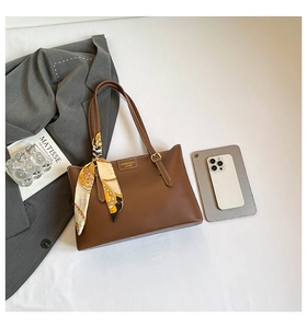 Detail of a brown leather tote bag with a patterned silk scarf and fashion metal plaque