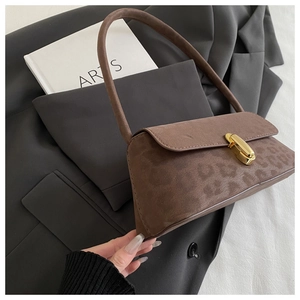 Detail of leopard print suede shoulder bag with gold metal clasp on a grey blazer