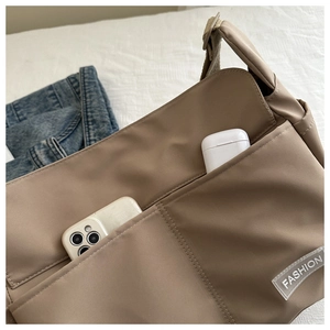 Close-up of khaki nylon messenger bag with front pockets and fashion tag detail