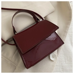 Macro detail of glossy burgundy patent leather bag showing fine stitching and top handle
