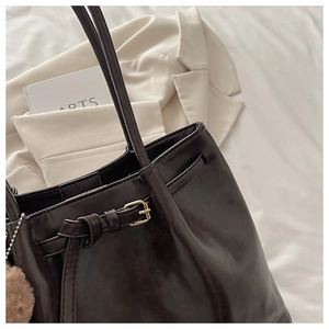 Detail of dark faux leather tote bag showing side buckle and plush charm accessory