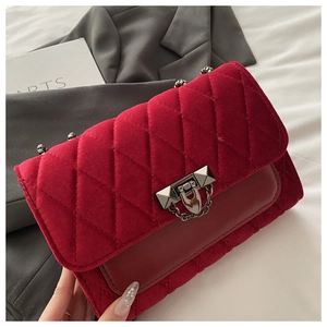 Close-up of red velvet quilted bag with silver buckle on a grey blazer background