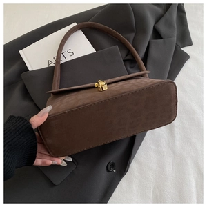 Detail shot of a vintage dark brown suede handbag featuring a gold square twist lock closure