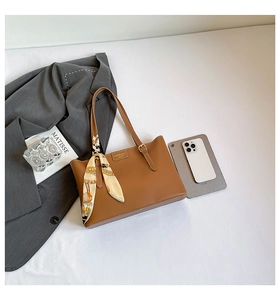 Detail view of a brown leather tote bag with an elegant silk scarf on the handle