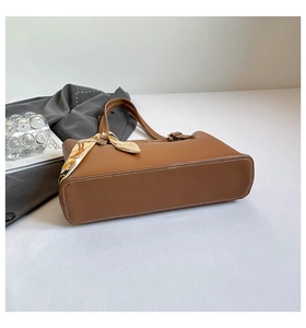 Detail of brown leather tote bag with contrast stitching and decorative silk scarf handle