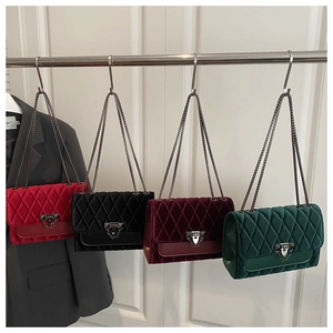 Quilted velvet chain bags in black, red, and green hanging on a display stand