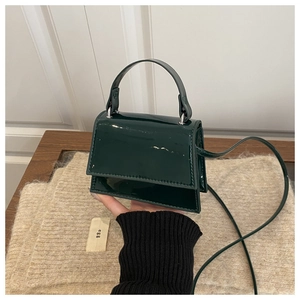 Detail of a dark green patent leather mini handbag with a top handle and shoulder strap