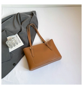 Detail of brown leather tote bag featuring U-shaped stitching and gold hardware buckle