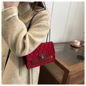 Detail of red quilted velvet handbag featuring a retro metal lock and chain strap