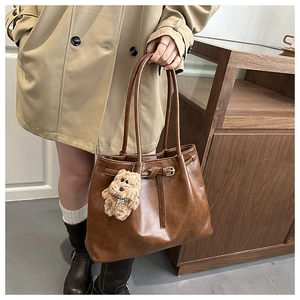 Detail of retro brown PU leather tote bag featuring metal buckle and plush bear charm